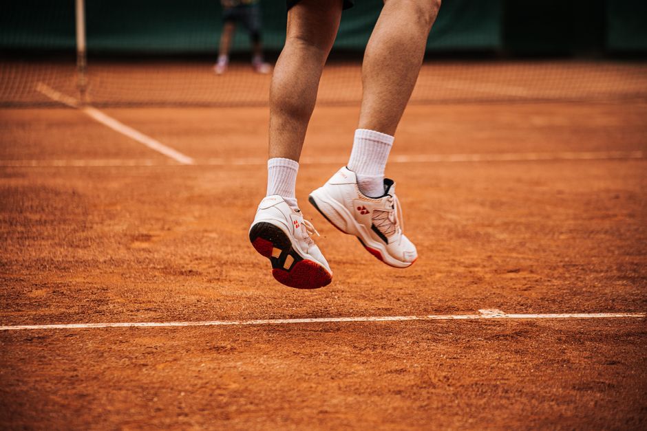 Imagem de um atleta de tênis em movimento durante uma partida, destacando a agilidade e o esforço físico no esporte.