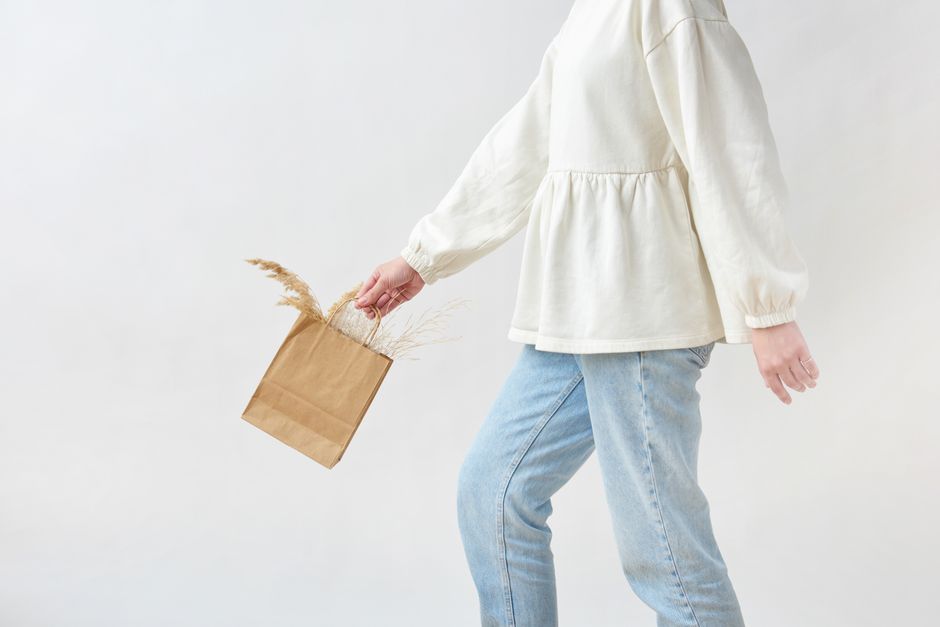 Imagem de uma pessoa segurando uma sacola de papel com grama seca, simbolizando sustentabilidade e consumo consciente.