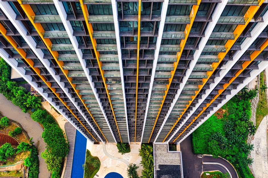 Imagem de um arranha-céu visto de cima, destacando sua estrutura moderna e o entorno próximo de áreas verdes, simbolizando urbanismo e arquitetura contemporânea.