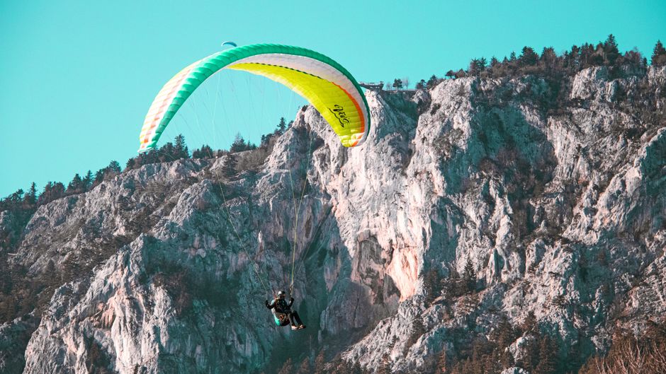 Pessoa praticando parapente sobre uma formação rochosa, destacando aventura e adrenalina na natureza