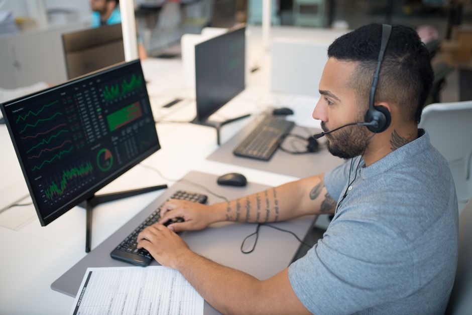 Analista financeiro monitorando gráficos e dados em ambiente de escritório, focado em análise de mercado ou desempenho financeiro.