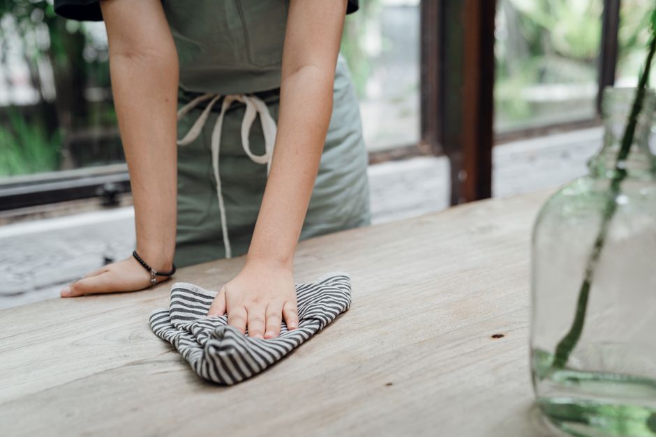 Pessoa limpando uma mesa de madeira com um pano em ambiente que remete a um espaço de convivência ou trabalho sustentável.