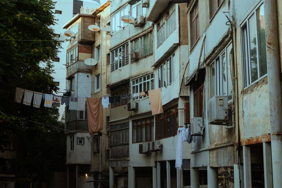 Imagem de edifícios residenciais antigos com varandas, roupas penduradas e sinais de desgaste na fachada, representando a vida em áreas urbanas de baixa renda.