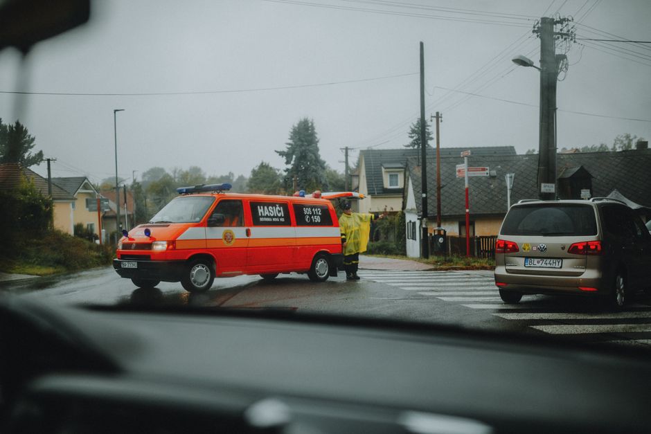 Imagem de uma emergência de incêndio na rua, vista de dentro de um carro, com uma viatura de bombeiros e uma equipe atendendo a ocorrência.