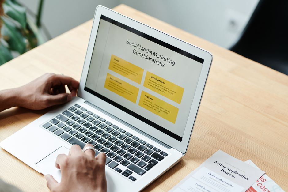 Pessoa analisando uma apresentação sobre marketing nas redes sociais em um laptop, numa mesa de trabalho moderna.