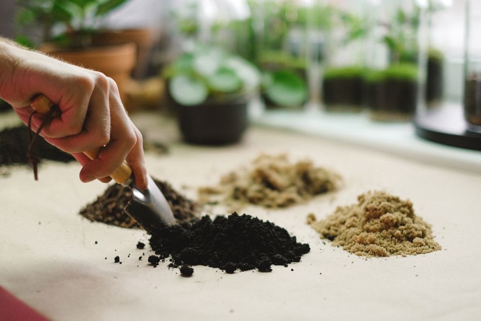 Pessoa manipulando solo ou substrato em um ambiente de cultivo ou horticultura, com foco na preparação do solo.