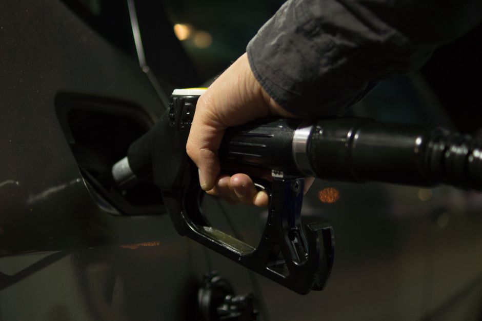 Pessoa abastecendo um carro com um galão de combustível em um posto, destacando o tema de abastecimento veicular.