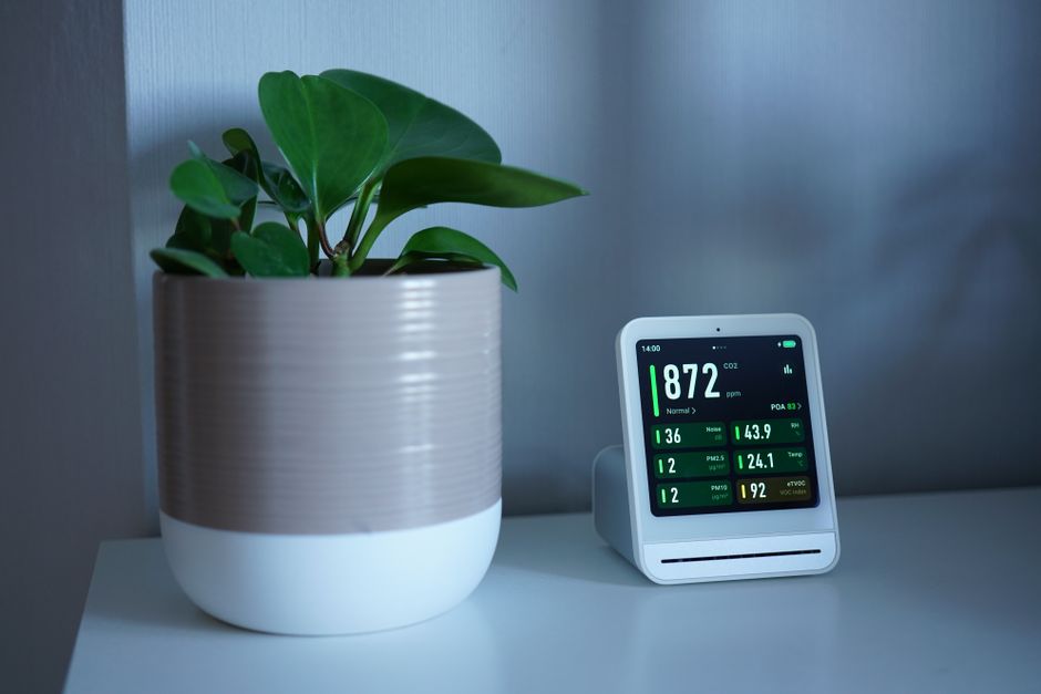 Imagem de um ambiente de escritório com uma planta decorativa ao lado de um aparelho medidor de qualidade do ar, destacando a importância do bem-estar no trabalho.