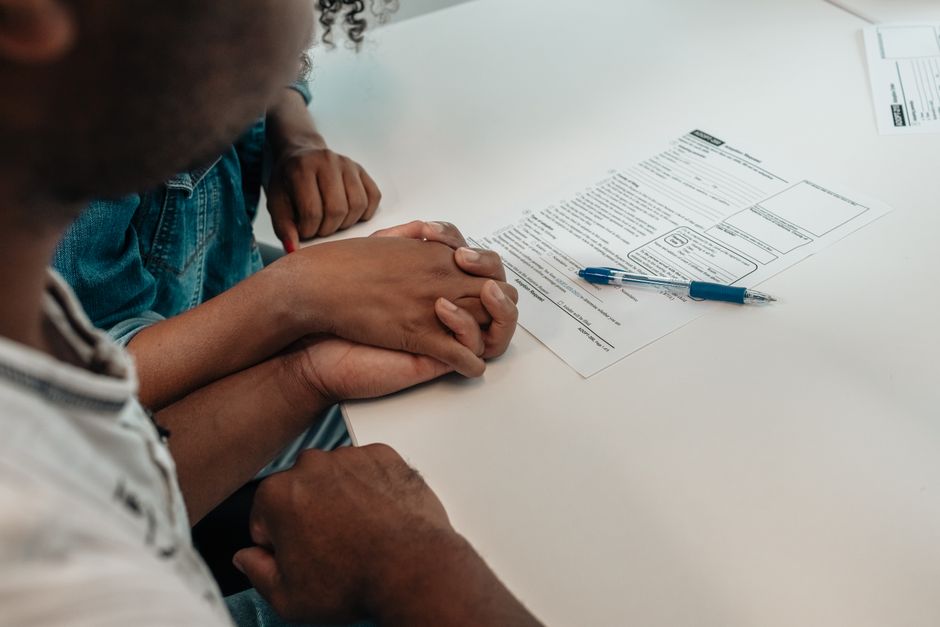 Duas pessoas segurando as mãos de forma apoio e solidariedade durante assinatura de documentos no ambiente de uma reunião ou consulta legal.