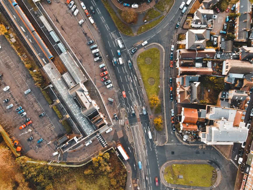 Imagem aérea de uma área urbana com ruas, calçadas, veículos e prédios, capturando o movimento e a estrutura de uma cidade.