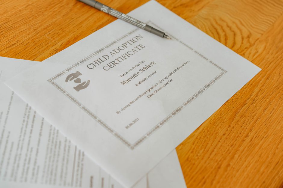 Certificado de adoção de criança sobre uma mesa de madeira com caneta ao lado, simbolizando documentação e processos oficiais relacionados à adoção infantil.