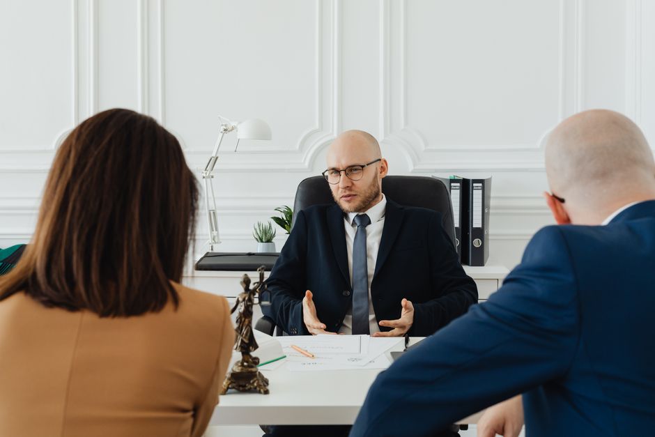 Homem em reunião de negócios explicando estratégias para duas pessoas em ambiente de escritório elegante.