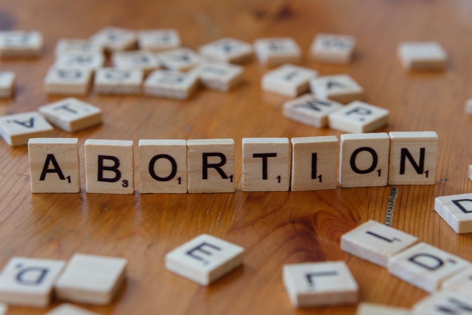 Palavras de blocos de arrasar que formam o tema do aborto, com elementos dispersos ao redor em uma superfície de madeira, simbolizando debate e controvérsia.