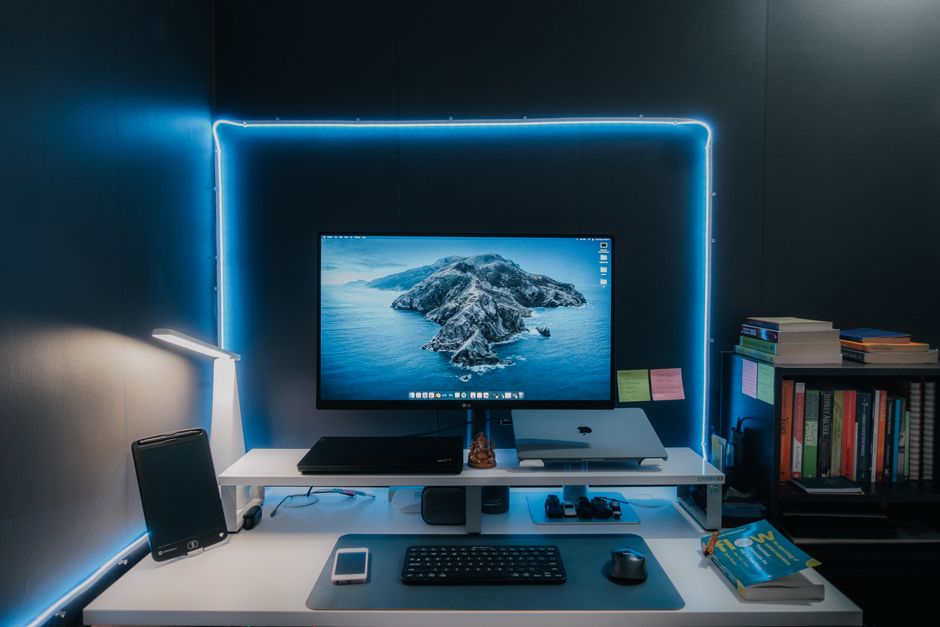 Imagem de um ambiente de trabalho moderno com computador de tela grande, iluminação de LED azul e livros organizados, ideal para artigos sobre produtividade e tecnologia no home office.