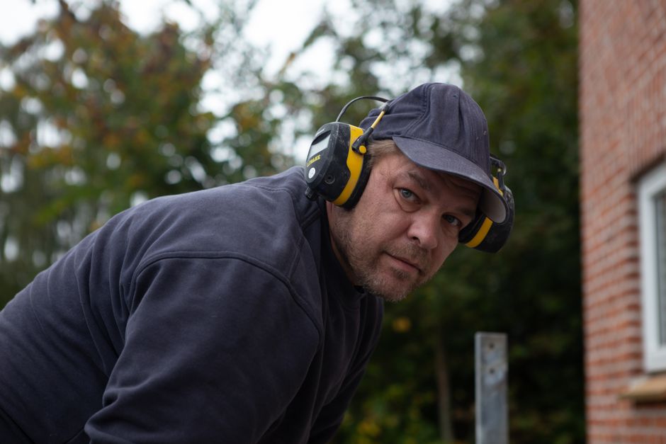 Homem em atividade ao ar livre usando protetores auriculares, possivelmente trabalhando em construção ou manutenção, com foco na segurança no ambiente externo.