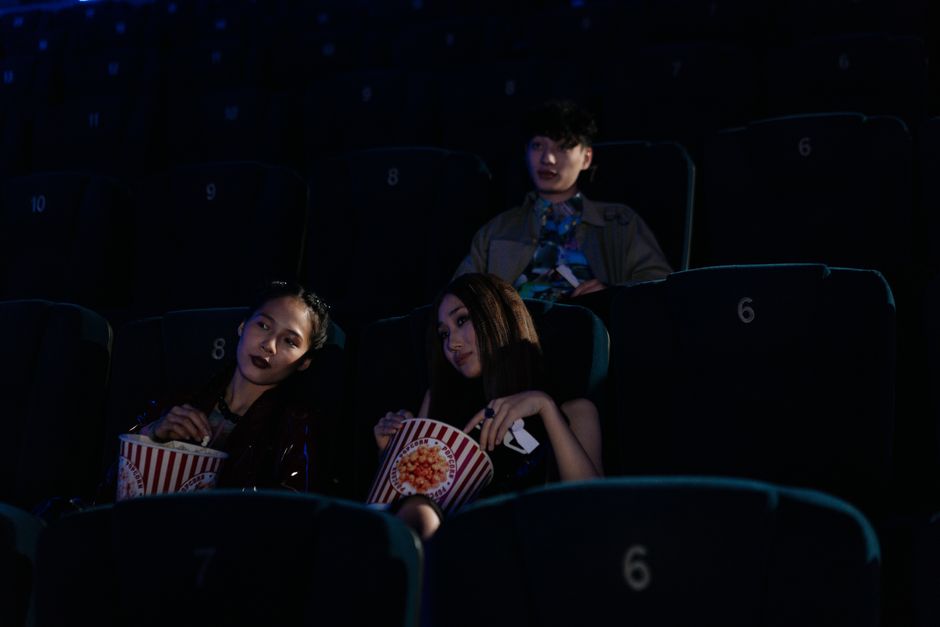 Pessoas assistindo a um filme em uma sala de cinema escura, com expressão de interesse e relaxamento.