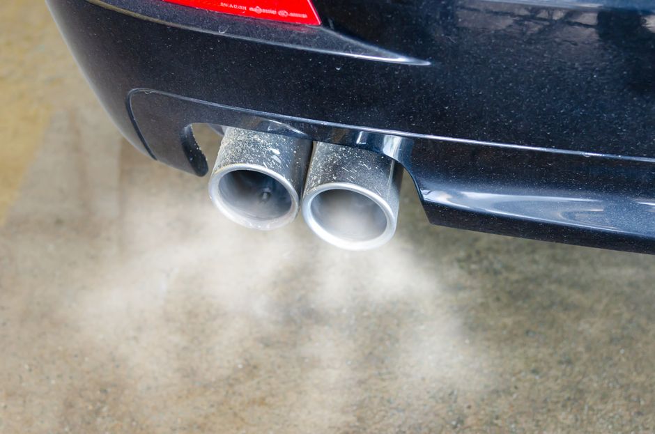 Imagem de um escapamento de carro emitindo fumaça densa, simbolizando poluição ambiental e emissão de gases poluentes.