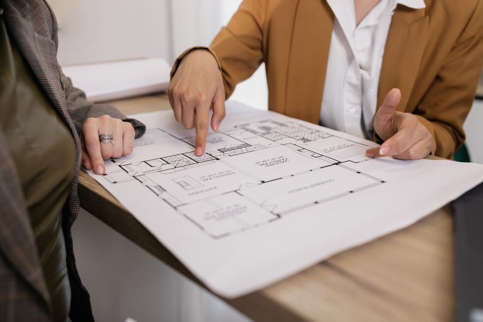 Pessoas discutindo detalhes de um projeto de arquitetura ou construção em uma mesa de escritório.