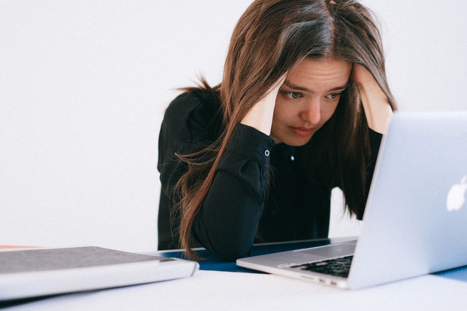 Mulher com expressão de preocupação e estresse ao usar um notebook, representando desafios e ansiedade no ambiente de trabalho ou estudos.