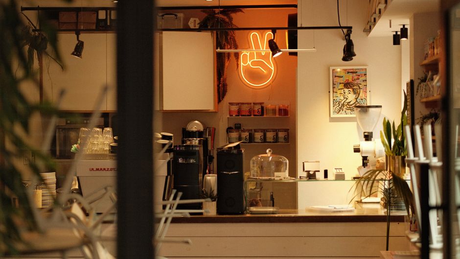 Imagem de um café moderno com decoração acolhedora, iluminação suave e elementos que sugerem um ambiente perfeito para encontros ou trabalho criativo.