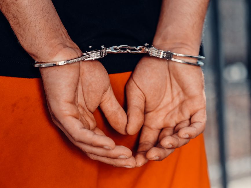 Pessoa presa em flagrante com algemas nas mãos, representando criminalidade ou segurança pública.