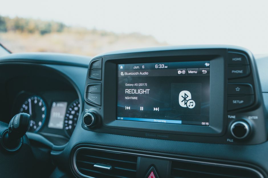 Tela de sistema de entretenimento no painel de um carro, exibindo informações sobre uma playlist e conexão Bluetooth, durante uma viagem por estrada.