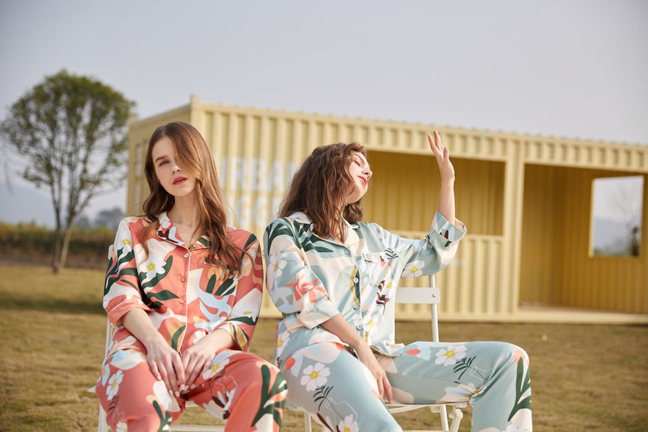 Duas mulheres sentadas ao ar livre usando roupas de pijama com estampas florais, transmitindo um momento de lazer e conforto na natureza.