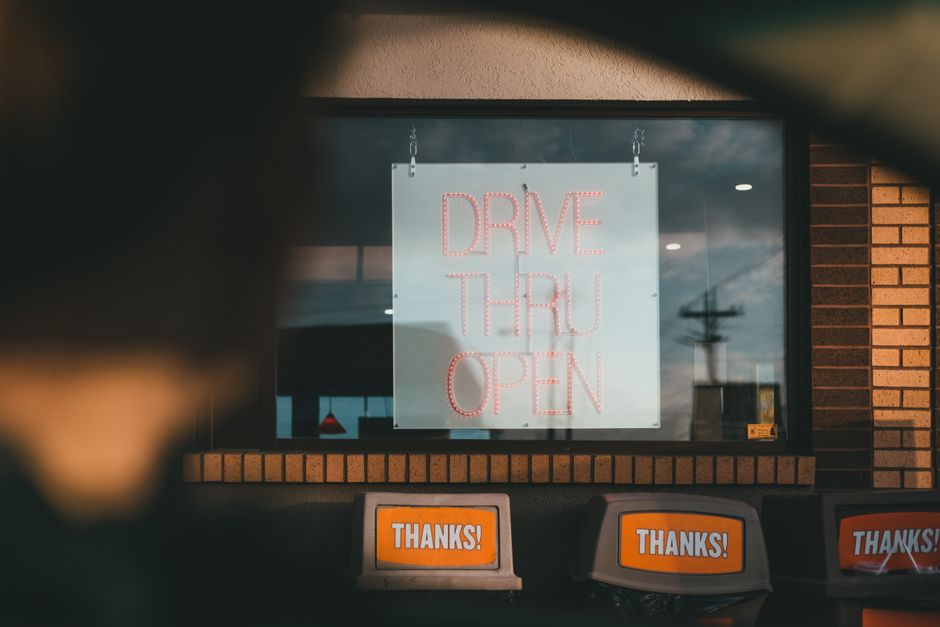Vitrine de restaurante com sinal de drive-thru aberto à noite, vista de dentro do estabelecimento.