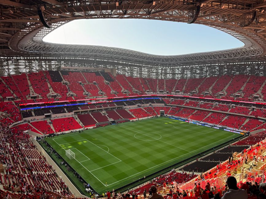 Interior de um estádio de futebol moderno, pronto para uma partida, com arquibancadas e gramado bem cuidados.