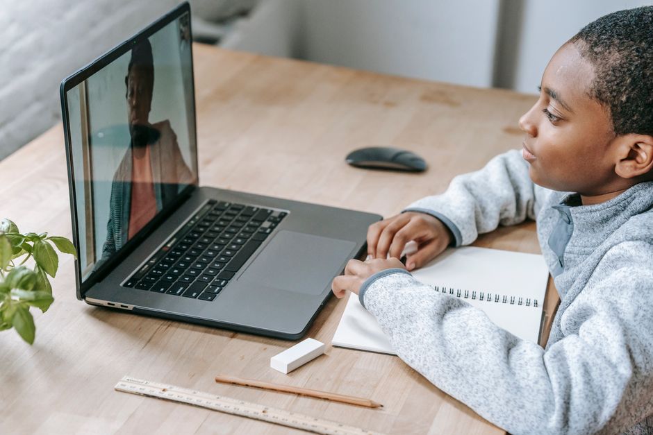 Menino participando de uma aula online ou reunião virtual, com recursos escolares ao lado, representando educação digital ou aprendizagem remota.