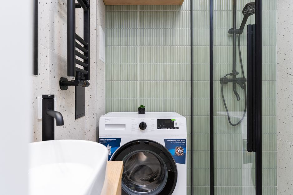 Imagem de uma área de lavanderia moderna com máquina de lavar, chuveiro e detalhes decorativos minimalistas.