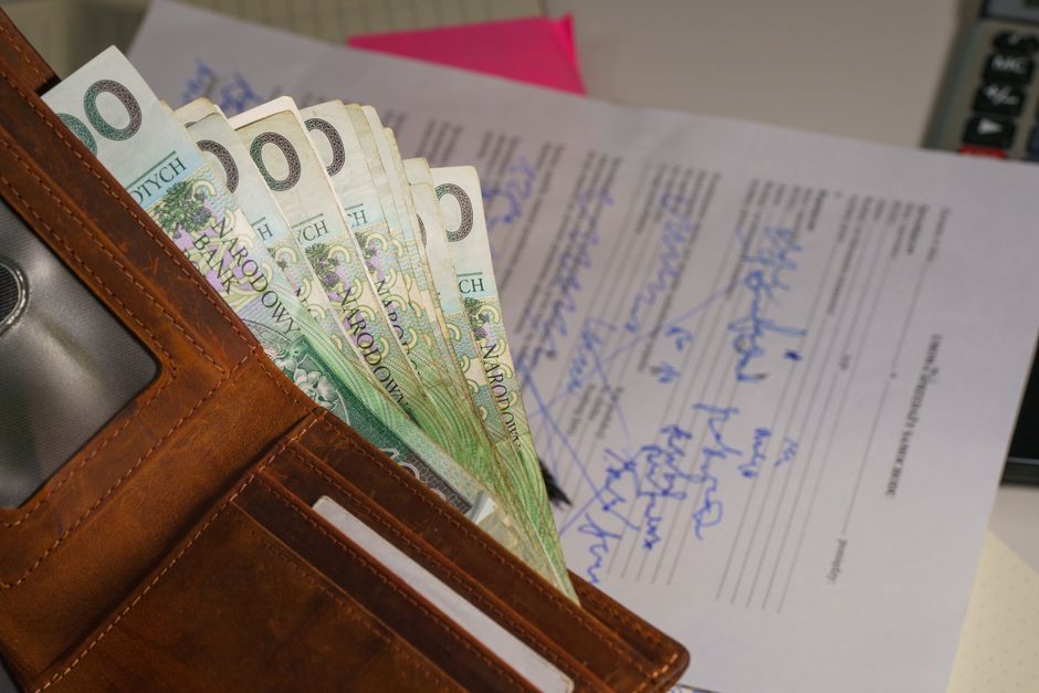 Imagem de uma carteira com cédulas de dinheiro em cima de documentos financeiros, representando planejamento financeiro e gestão de finanças pessoais ou empresariais.