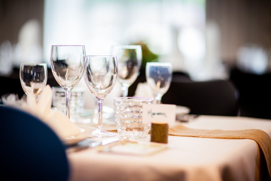 Imagem de uma mesa de jantar preparada para um evento ou celebração formal, com taças de vidro e utensílios elegantes, em um ambiente bem iluminado e acolhedor.