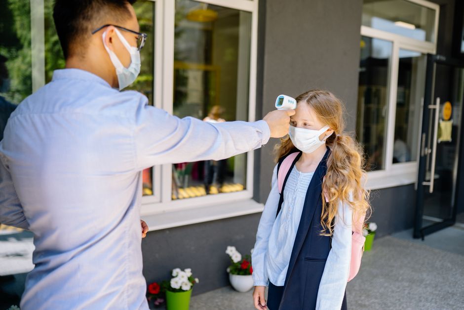 Criança sendo medida a temperatura por um profissional de saúde ao entrar na escola, em meio à pandemia de COVID-19.