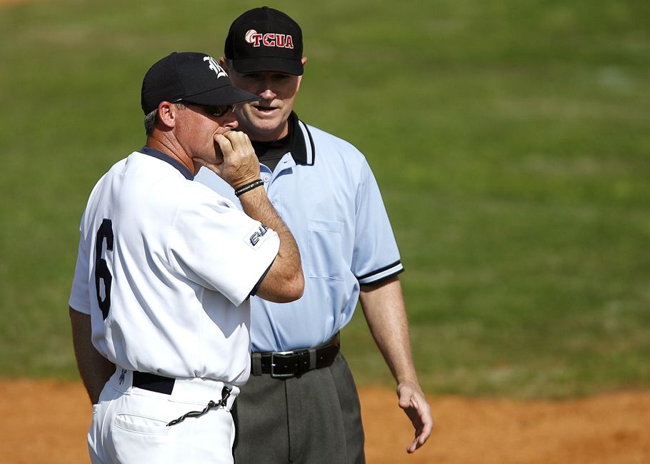 Treinador de beisebol conversando com umpire durante jogo ao ar livre.