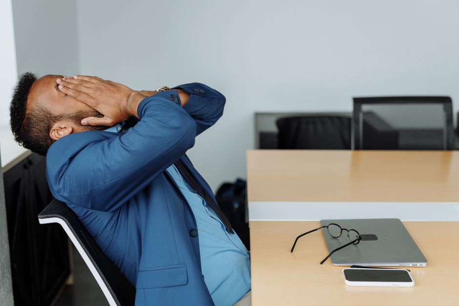 Homem de terno azul expressando cansaço ou alívio em ambiente de escritório, simbolizando o esgotamento relacionado ao trabalho ou ao estresse profissional.