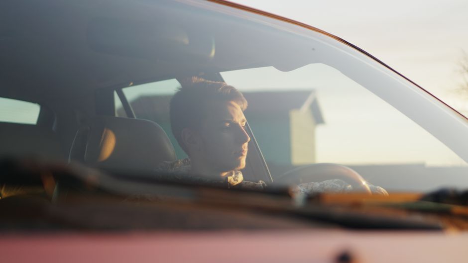 Homem dirigindo um carro ao entardecer, transmitindo uma sensação de reflexão ou viagem.