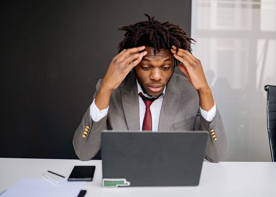 Homem de terno tentando resolver um problema ou dúvida com expressão de preocupação diante do computador em ambiente de escritório.