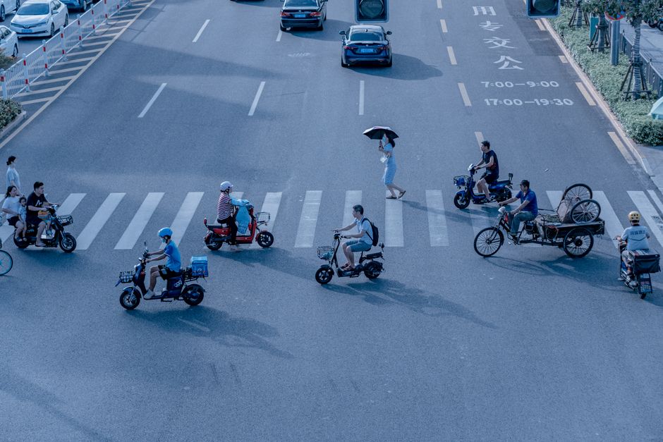 Imagem de um cruzamento urbano com pedestres, ciclistas e motoristas convivendo em harmonia, mostrando um ambiente de transporte diversificado e sustentável.