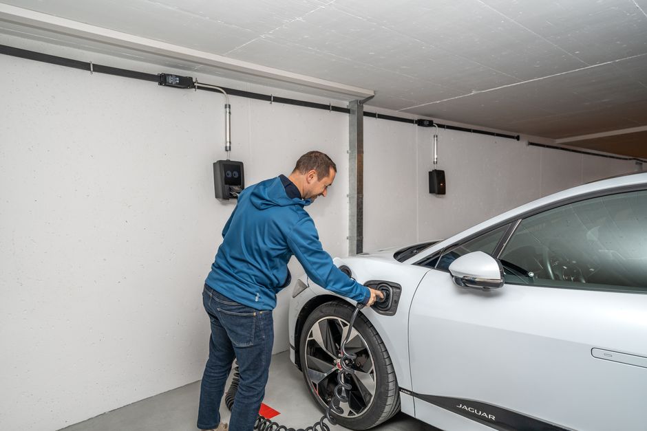 Homem carregando um carro elétrico em uma garagem moderna, destacando a preocupação com sustentabilidade e consumo de energia.