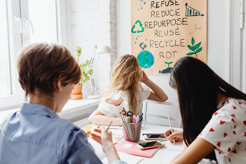 Três pessoas participando de uma discussão sobre sustentabilidade e práticas ecológicas em um ambiente de escritório ou sala de estudo.