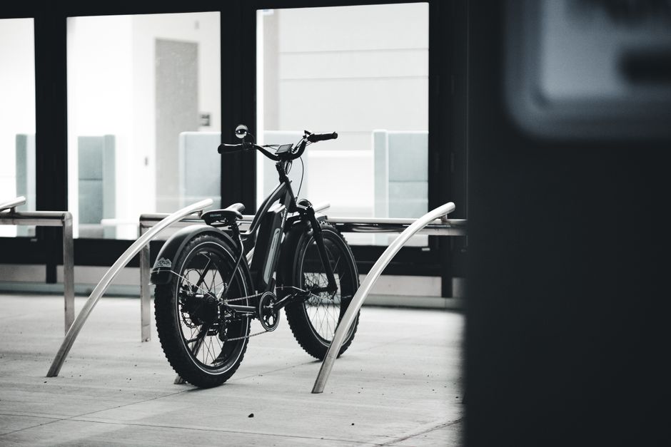 Imagem de uma bicicleta estacionada em um bicicletário em um ambiente urbano moderno, sugerindo mobilidade sustentável e transporte alternativo.