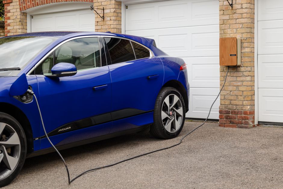 Carro elétrico carregando na parede de uma casa, destacando a adoção de veículos sustentáveis e tecnologia de carregamento doméstico.