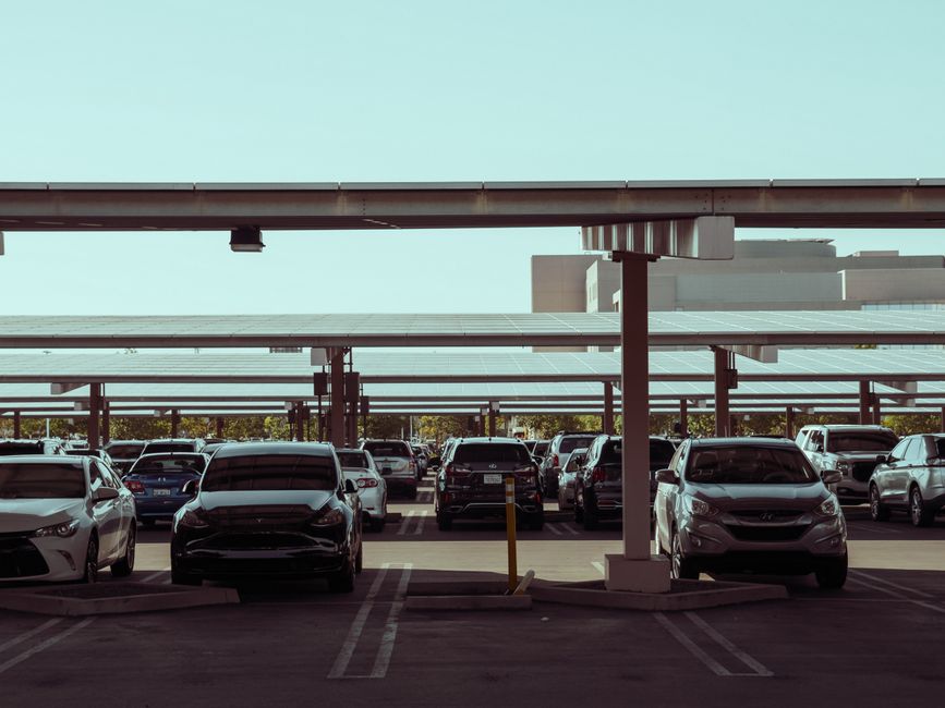 Imagem de um estacionamento com várias vagas ocupadas e cobertura solar, representando mobilidade urbana ou planejamento de infraestrutura.