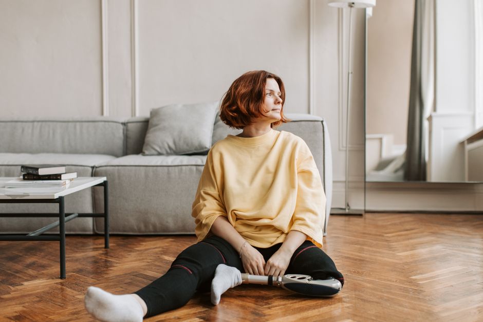 Mulher relaxando no chão de uma sala moderna, usando aspirador de pó, representando bem-estar e cuidado com o lar.
