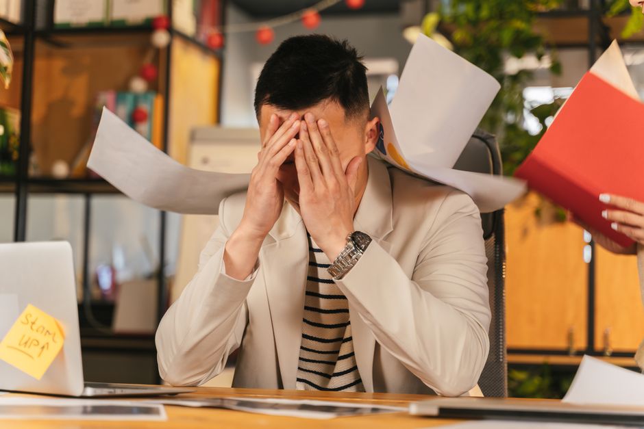 Homem sobrecarregado de trabalho em ambiente de escritório, simbolizando estresse e excesso de tarefas.