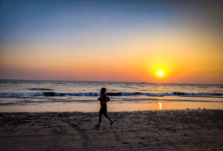 Pessoa caminhando na praia durante o pôr do sol, transmitindo tranquilidade e reflexão.