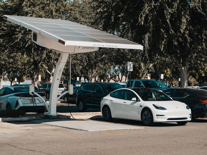 Carro elétrico sendo carregado em uma estação de carregamento solar em estacionamento ao ar livre, promovendo energia renovável e sustentabilidade.