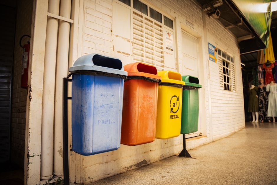 Imagem de lixeiras coloridas para separação de resíduos, simbolizando sustentabilidade e gestão de lixo em ambientes urbanos.