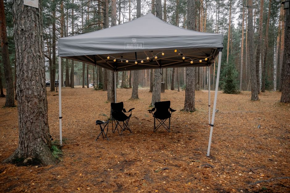 Área ao ar livre montada com uma tenda em meio a uma floresta, ideal para eventos ou encontros na natureza.